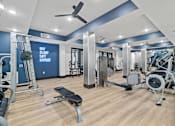 Thumbnail 19 of 33 - A gym with a variety of equipment including a weight bench, a treadmill, and a fan.