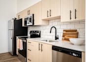 Thumbnail 16 of 30 - The Wes Gresham Oregon Apartments kitchen counter with bright wood cabinets and stainless steel applicances