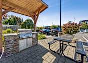 Thumbnail 10 of 28 - A picnic area with a grill and a table under a wooden roof.