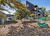 Thumbnail 13 of 28 - A playground with a green swing set in front of a modern building.