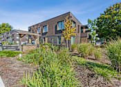 Thumbnail 27 of 28 - A modern house with a brown exterior and a well-maintained garden in front.