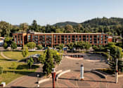Thumbnail 27 of 27 - Arts Plaza Gresham Oregon Apartments building exterior with parking and courtyard.