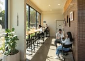 Thumbnail 7 of 27 - Arts Plaza Gresham Oregon Apartments A man and woman are sitting at a table in a brightly lit room with a potted plant on the left and a brick wall on the right.