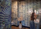 Thumbnail 19 of 27 - Arts Plaza Gresham Oregon Apartments A woman is brushing her teeth in a bathroom with a wallpapered shower area.