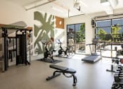 Thumbnail 5 of 27 - Arts Plaza Gresham Oregon Apartments fully equipped fitness center with a woman working out on a treadmill.