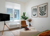 Thumbnail 22 of 30 - The Wes Gresham Oregon Apartments  leather chair with white ottoman and a green couch. Art on wall