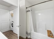 Thumbnail 29 of 38 - A white bathroom with a tub, towel rack, and a washing machine.