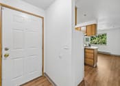 Thumbnail 6 of 25 - A white door with a gold handle is on the left of a room with a wooden floor.