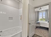 Thumbnail 6 of 33 - A white bathroom with a tub and a bedroom with a bed.