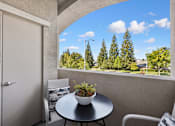 Thumbnail 21 of 28 - A balcony with a table and chairs overlooking a tree-filled landscape.