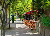 Thumbnail 31 of 35 - A row of wooden tables are lined up under a red awning.