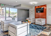 Thumbnail 18 of 29 - A living room with a white couch, a white chair, a white ottoman, a blue rug, a wooden cabinet, a flat screen TV, and a window with a view of the outside.