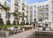 Thumbnail 4 of 28 - Hollywood CA Apartments - The Fifty Five Fifty - An Outdoor Courtyard At The Base Of The Building With Multiple Lounge Areas, A BBQ Area, And Beautiful Landscaping