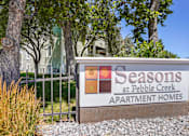 Thumbnail 10 of 10 - A sign for Seasons at Pebble Creek Apartment Homes is in front of a fence and trees.