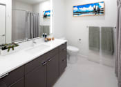Thumbnail 6 of 35 - A bathroom with a white countertop and a painting of a beach scene on the wall.