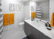 Thumbnail 14 of 35 - A bathroom with a white sink and toilet, a grey cabinet, and a mirror.