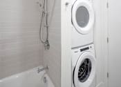 Thumbnail 7 of 35 - A white washing machine is in a bathroom next to a bathtub.