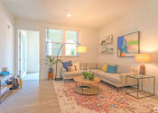 Thumbnail 23 of 28 - A living room with a couch, coffee table, and a painting on the wall.
