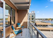 Thumbnail 5 of 30 - A balcony with a blue chair and a table is overlooking a body of water.