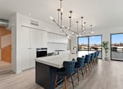 Thumbnail 17 of 30 - A modern kitchen with a long white island and blue chairs.