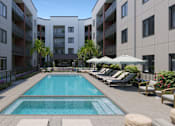Thumbnail 8 of 9 - A large swimming pool in the middle of a courtyard surrounded by lounge chairs and umbrellas.