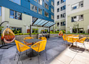 Thumbnail 26 of 28 - an outdoor patio with yellow chairs and tables at an apartment building