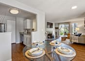 Thumbnail 14 of 30 - View of dining room, kitchen, and living room with white walls, fireplace, and wood-style flooring at Cedar Crest Apartments in West Beaverton, Oregon.