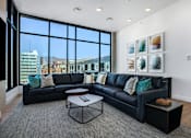 Thumbnail 10 of 22 - A black leather sofa with a grey rug and a coffee table in front of a window.