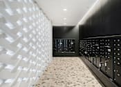 Thumbnail 17 of 22 - A hallway with a white patterned wall and a black wall with a number of buttons.