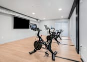 Thumbnail 14 of 22 - A room with a row of stationary bikes and a monitor on the wall.