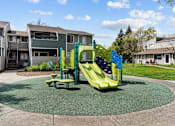 Thumbnail 15 of 26 - A playground with a green and yellow slide in the middle of a grassy area.