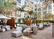 Thumbnail 6 of 28 - Dog-Friendly Apartments in Hollywood, CA - The Fifty Five Fifty - Courtyard with Palm Trees, White Outdoor Furniture, and Tall Wooden Dividers