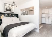 Thumbnail 1 of 12 - a bedroom with a bed and a kitchen in the background