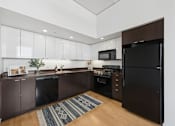 Thumbnail 2 of 18 - A kitchen with brown cabinets and a black refrigerator.