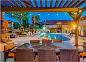 Thumbnail 15 of 24 - A poolside area with a table and chairs under a canopy.