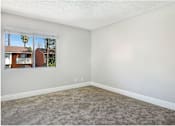 Thumbnail 4 of 24 - A room with a carpeted floor and a window showing a view of a house and trees outside.