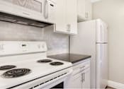 Thumbnail 6 of 24 - A white stove top oven with a white microwave above it and a white refrigerator to the right.