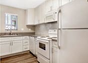 Thumbnail 5 of 24 - A white refrigerator stands in a kitchen with white cabinets and a white stove.