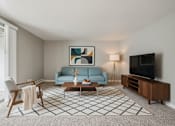 Thumbnail 3 of 22 - A living room with a blue couch, a coffee table, a chair, a painting, a lamp, and a television.
