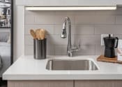 Thumbnail 19 of 33 - a kitchen sink with white countertops and a white shelf above it with two bottles of beer