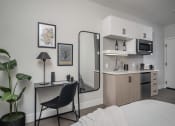 Thumbnail 28 of 33 - a bedroom with a bed and a desk with a mirror in front of it and a kitchen