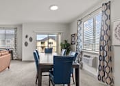 Thumbnail 3 of 24 - A living room with a brown sofa, a dining table with blue chairs, and a view of a building through the window.