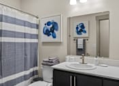 Thumbnail 11 of 24 - A bathroom with a striped shower curtain and two blue abstract paintings on the wall.