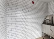 Thumbnail 22 of 24 - A white tiled wall with a red fire alarm on it.