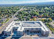 Thumbnail 1 of 23 - A large apartment complex with a swimming pool is surrounded by trees and roads.
