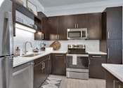 Thumbnail 21 of 23 - A modern kitchen with dark brown cabinets and stainless steel appliances.