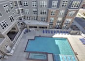 Thumbnail 8 of 23 - A large swimming pool is surrounded by a patio with lounge chairs and a stone building with a balcony.