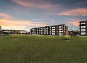 Thumbnail 22 of 43 - A large grassy field in front of a building with a sunset in the background.