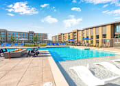 Thumbnail 2 of 43 - A swimming pool with sun loungers and apartment buildings in the background.
