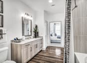 Thumbnail 28 of 43 - A bathroom with a white toilet, a wooden vanity, and a shower with a curtain.
